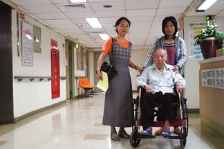 Two Women Pushing an Elderly Man in a Wheelchair