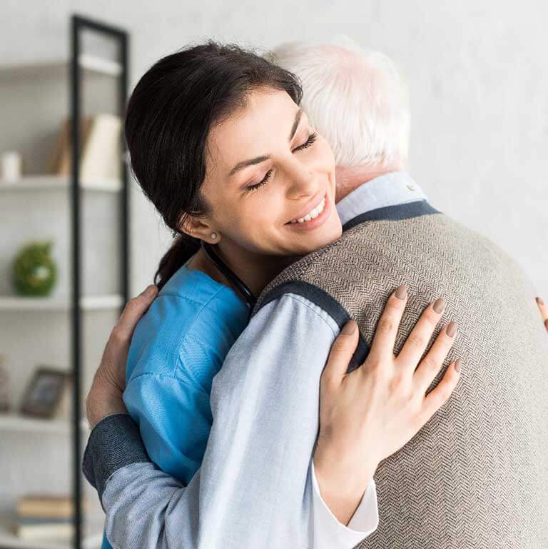 A warm embrace between a caregiver in blue scrubs and an elderly person, symbolizing compassionate home care and senior assistance services provided by dedicated professionals.
